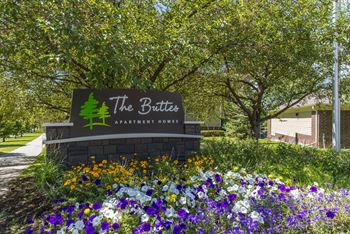 A sign for The Butter Apartment Home is surrounded by flowers  at The Buttes Apartments Loveland, CO.